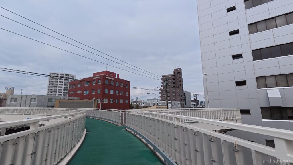 初春の空に円を描く菊水歩道橋。4差路の交差点を、巨大な鉄骨の輪が包み込むように架かっている。