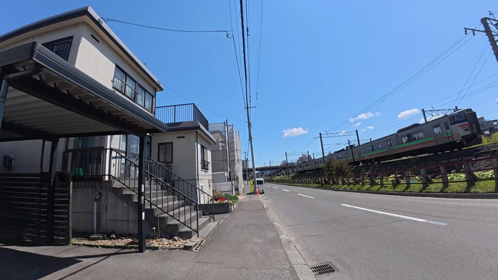 青空の下、一直線の道路のすぐ横を颯爽と駆け抜けるJRの電車